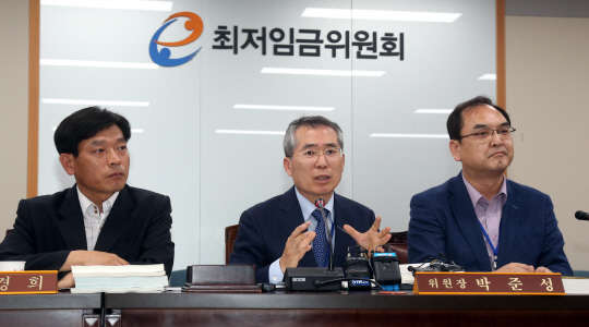 박준성 최저임금위원장이 9일 새벽 정부세종청사    최저임금위원회 전원회의실에서 내년도 최저임금 시급이 올해보다 8.1%(450원) 오른 6천30원으로 결정됐다고 밝히고 있다. 시급을 월급으로 환산하면 126만270원(월 209시간 기준)이 된다. 왼쪽은 류경희 부위원장, 오른쪽은 이장원 공익위원 간사.